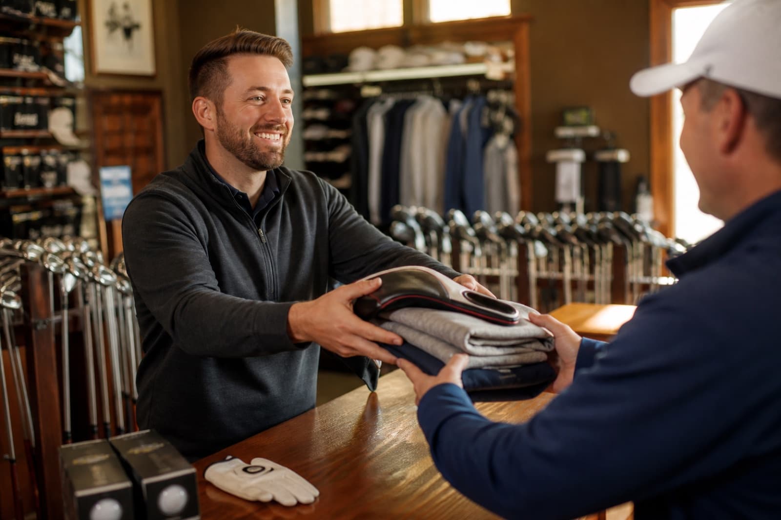 A pro-shop staff member handing a member new golf gear and apparel